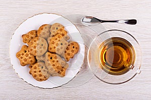 Figured cookies in plate, tea in cup on saucer, spoon on table. Top view
