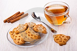 Figured cookies in saucer, cinnamon, tea in cup, teaspoon on table