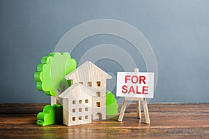 Figures of houses and an easel sign for sale. Buying and selling real estate, hot offers and property valuation. Smart investments