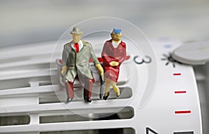 Figures of old retired couple sitting warmly dressed on a heater thermostat at cold temperatures on saving clip