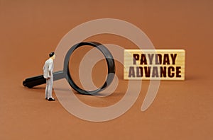 A figurine of a businesswoman looks through a magnifying glass at a block with the inscription - Payday Advance