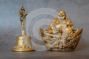 Figurine Cheerful Hotei  and golden bell close-up, soothing and meditative. Smiling Buddha and golden bell Isolated on gray