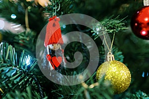 Figurine of a gnome in a hat with a heart in his hands hangs on a branch of a Christmas tree