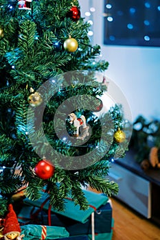 Figurine of a horse on skids hangs on a branch of a Christmas tree among colorful balls