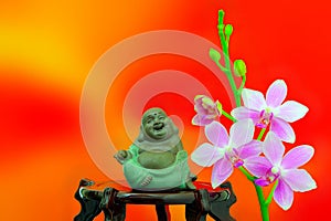 Figurine of laughing buddha and pink orchid flowers