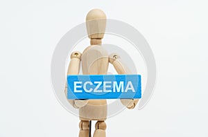 A figurine of a man holds in his hands a blue wooden block with the inscription ECZEMA. The figurine is out of focus