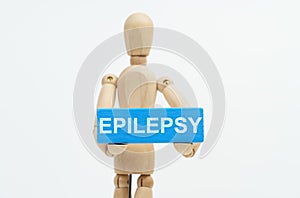 A figurine of a man holds in his hands a blue wooden block with the inscription EPILEPSY. The figurine is out of focus