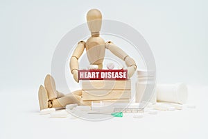 A figurine of a man sitting among pills lifts a red wooden block with an inscription HEART DISEASE from a wall of blocks