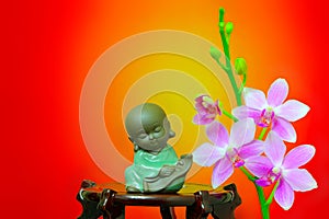 Figurine of meditating little buddha and pink orchid flowers