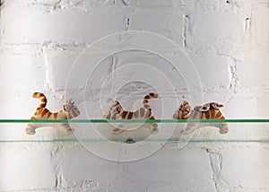 figurines of cute tigers on glass shelf against white wall