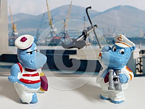 Figurines hippos of a sailor and a captain on the background of a sea anchor and port cranes. Kinderfilia