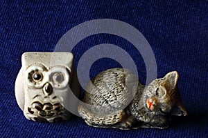 FIGURINES OF AN OWL AND A SLEEPING CAT ON BLUE CLOTH