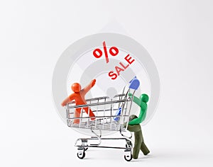 figurines of people made of plasticine are rolling a shopping cart with a poster painted for a discount. concept of discounts,