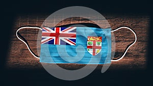 Fiji National Flag at medical, surgical, protection mask on black wooden background. Coronavirus Covidâ€“19, Prevent infection,