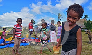 A Fijian young child in Navala, Fiji smiling looking into the camera with his fellow villagers behind