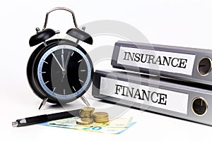File folders and alarm clock symbolize time pressure while working on finance and insurance
