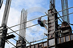 Filipino construction steel-man climbing down using scaffolding pipes on high-rise building