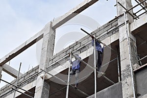 Filipino construction workers installing metal pipe scaffolds on high-rise building without protective suit.