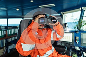 Filipino deck Officer on bridge of vessel or ship looking through binoculars