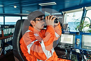 Filipino deck Officer on bridge of vessel or ship looking through binoculars