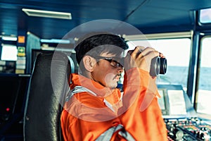 Filipino deck Officer on bridge of vessel or ship looking through binoculars