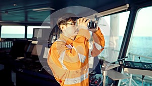 Filipino deck Officer on bridge of vessel or ship looking through binoculars