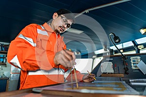 Filipino deck Officer on bridge of vessel or ship. He is plotting position on chart