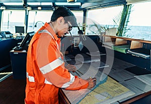 Filipino deck Officer on bridge of vessel or ship. He is plotting position on chart