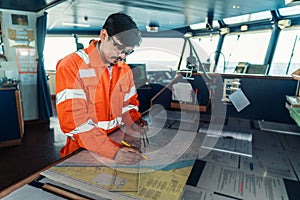 Filipino deck Officer on bridge of vessel or ship. He is plotting position on chart