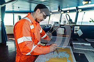 Filipino deck Officer on bridge of vessel or ship. He is plotting position on chart