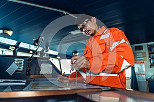 Filipino deck Officer on bridge of vessel or ship. He is plotting position on chart