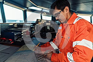 Filipino deck Officer on bridge of vessel or ship. He is plotting position on chart