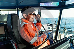 Filipino deck Officer on bridge of vessel or ship. He is speaking on GMDSS VHF radio