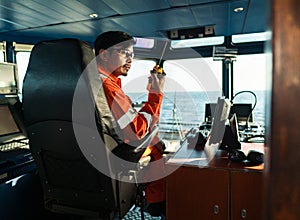 Filipino deck Officer on bridge of vessel or ship. He is speaking on GMDSS VHF radio
