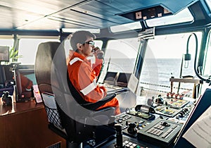 Filipino deck Officer on bridge of vessel or ship. He is speaking on GMDSS VHF radio photo