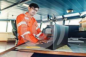 Filipino deck Officer on bridge of vessel or ship. He is using laptop, electronic paperwork at sea