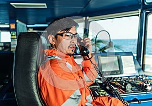 Filipino deck Officer on bridge of vessel or ship. He is speaking on GMDSS VHF radio photo