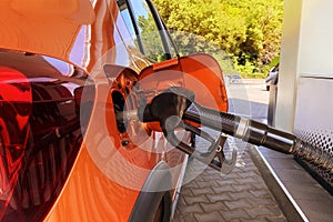 Fill car with fuel in petrol station. Pumping gasoline fuel in orange car at a gas station. Close up