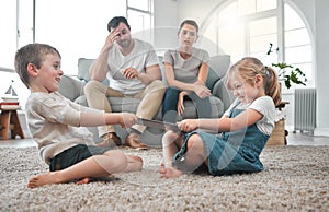 They fill our days with joy. two siblings fighting in a game of tug of war over their digital tablet.