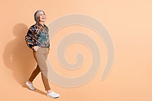 Fill size photo of pleasant nice pensioner woman dressed print shirt brown trousers go empty space isolated on pastel