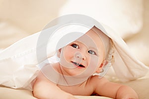 Filled curiousity. Cute baby boy lying under a sheet playfully and looking away.