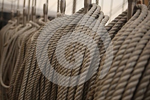 Filled frame background wallpaper photo of rows of beige plaited nautical tow ropes reeled together, hanging in lines on the deck