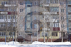 Filled frame full screen shot of an old ugly colorful facade of a soviet block house with windows, balconies and naked birches and