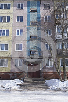 Filled frame full screen shot of an old ugly colorful facade of a soviet block house with windows, balconies and naked birches and