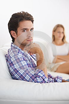 Filled with frustration - relationship issues. A upset man sitting in a sofa with hand on chin and upset wife sitting in
