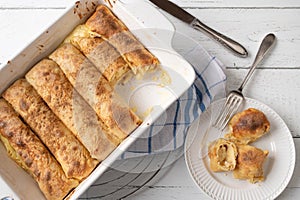 Filled pancake rolls with quark lemon filling in a baking dish on white background. flat lay