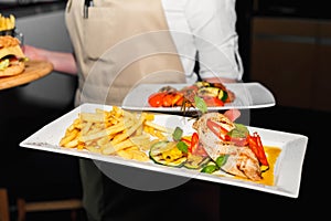 Fillet of fried chicken with French fries on a rectangular square white plate in the hand of an offspring close-up