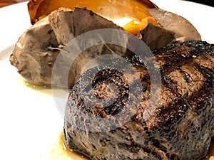 Fillet mignon with grill marks and sweet potato on a white plate