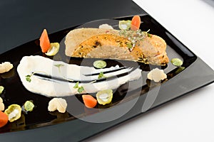 Fillet of red fish with vegetables, herbs and white sauce on a black glossy plate. Gourmet restaurant dish