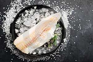 Fillet of white sea cold-water fish cod in ice cubes on a dark background. Top view